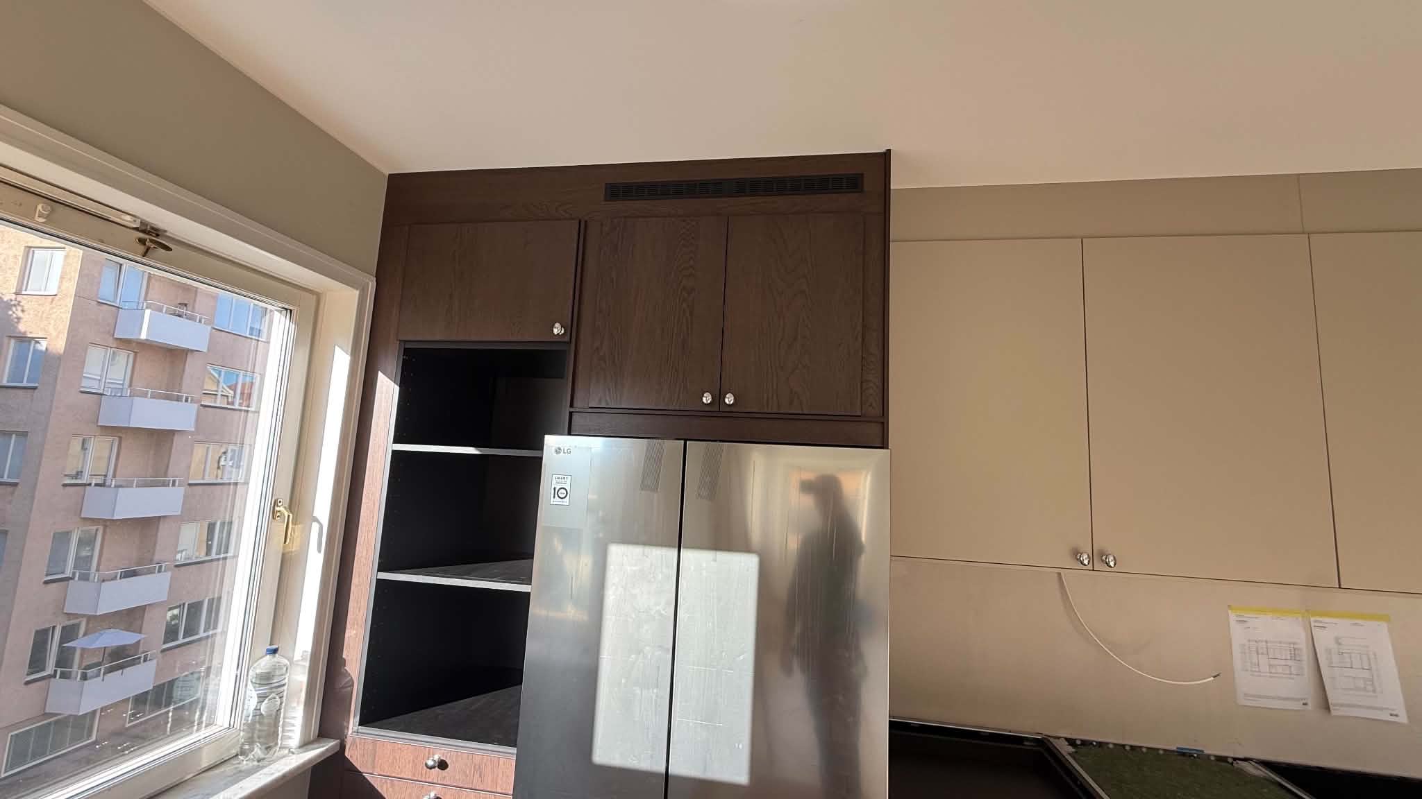 Högskåp med öppen hyllsektion och integrerat kylskåp i pågående köksrenovering