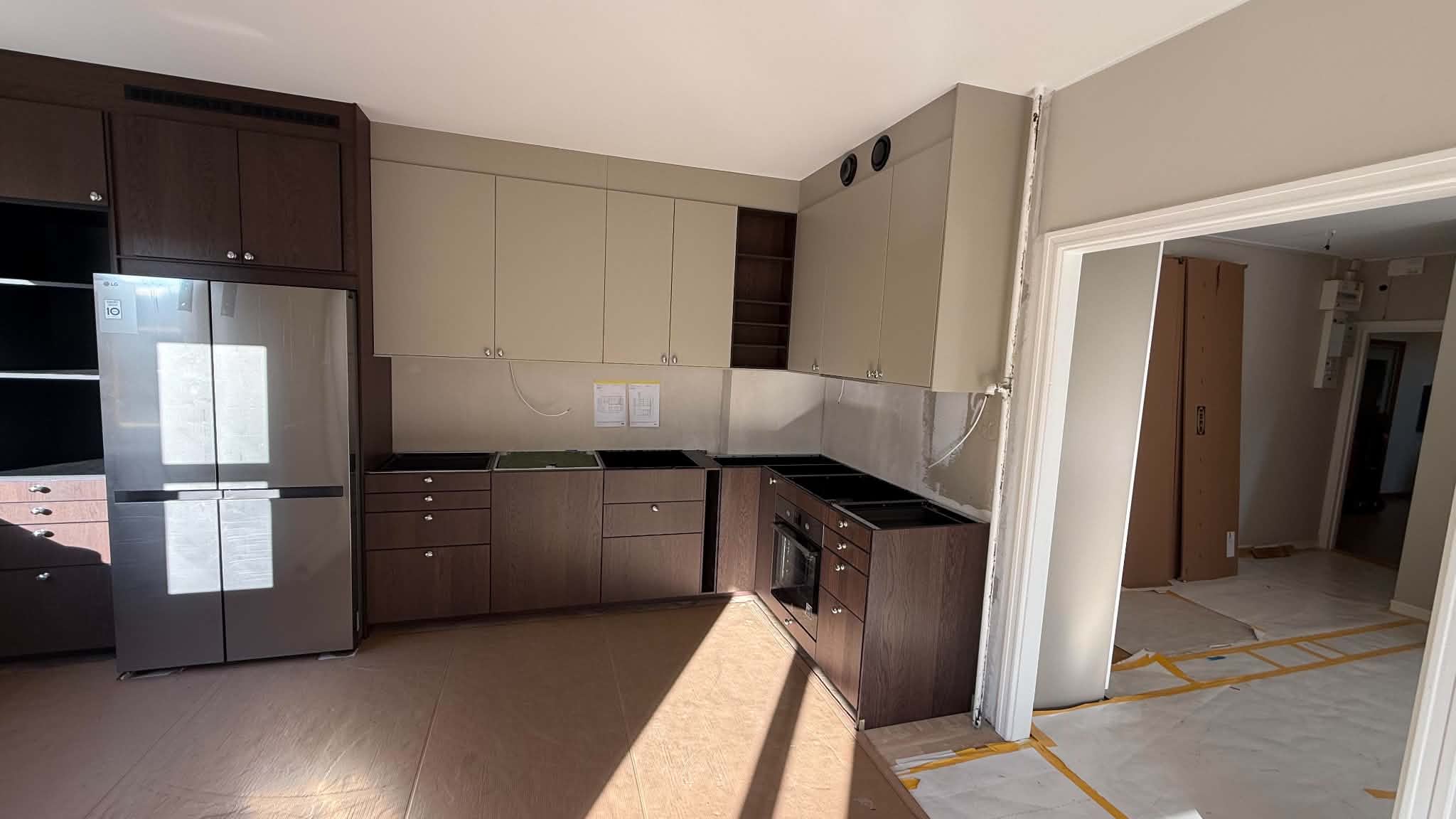 Vinkelkök under renovering med inbyggnadsugn, mörka luckor och plats för bänkskiva